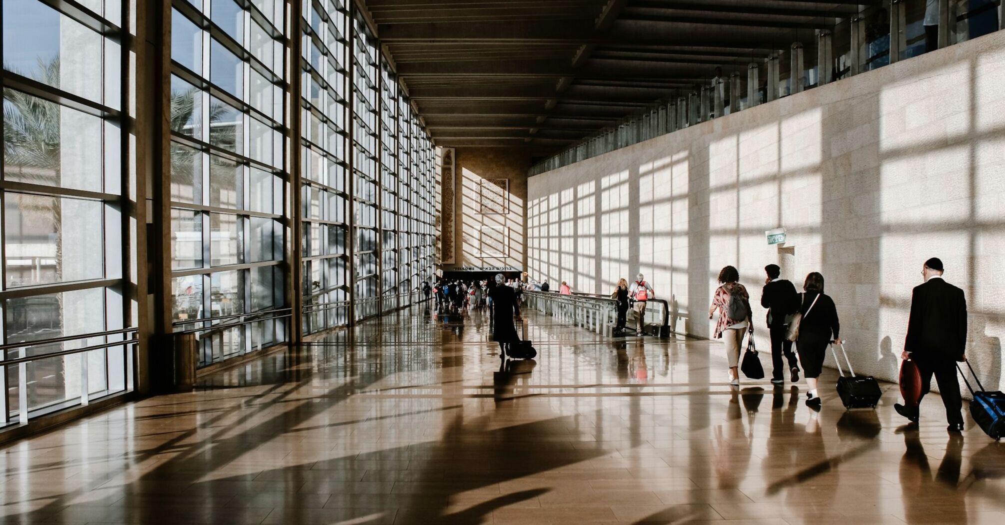 Passengers walking through a busy airport terminal with rolling luggage