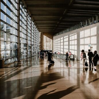 Passengers walking through a busy airport terminal with rolling luggage