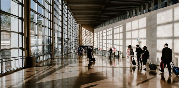 Passengers walking through a busy airport terminal with rolling luggage