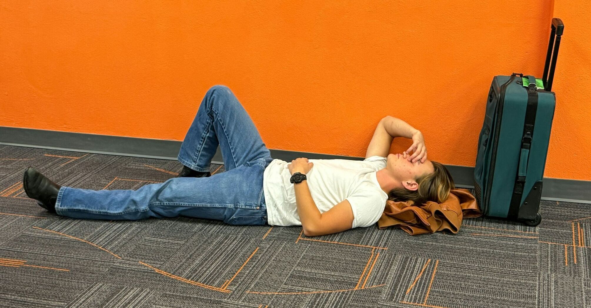 Traveller lying on airport floor beside suitcase during disruption