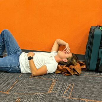 Traveller lying on airport floor beside suitcase during disruption
