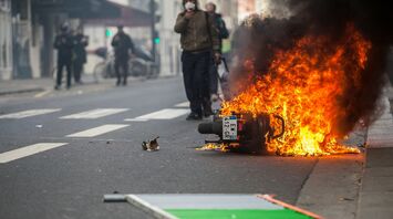 Motorcycle burning in city street during unrest with smoke and pedestrians nearby