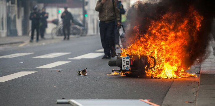 Motorcycle burning in city street during unrest with smoke and pedestrians nearby