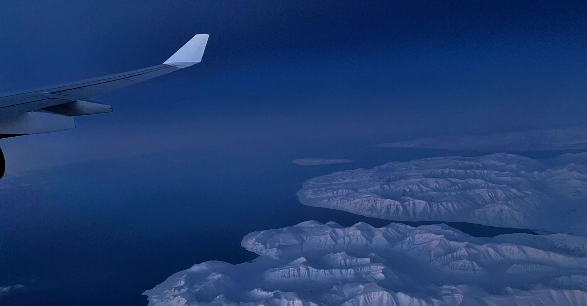 Aerial view of snow-covered Greenland coastline seen from aircraft window