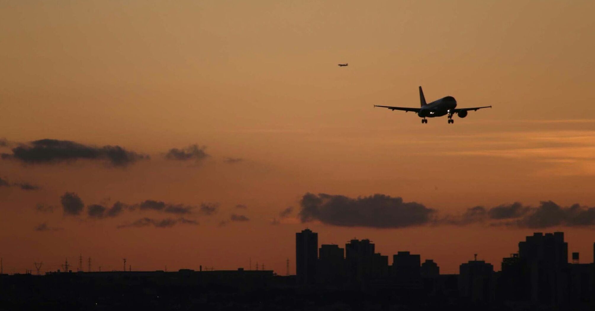 Airplane landing over city skyline at sunset