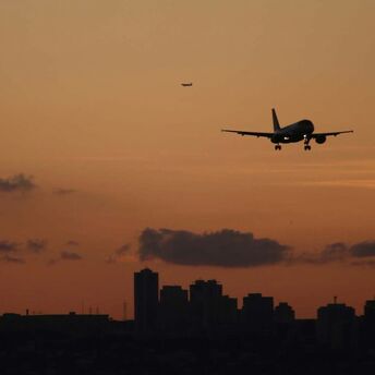 Airplane landing over city skyline at sunset
