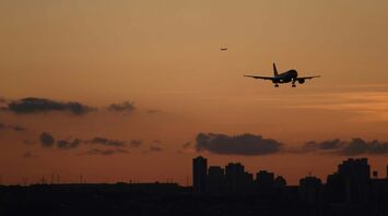 Airplane landing over city skyline at sunset