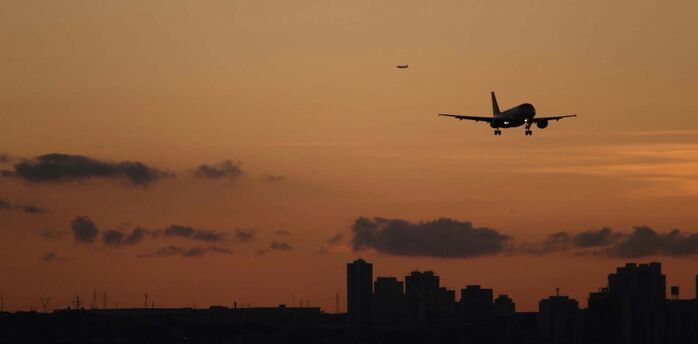 Airplane landing over city skyline at sunset