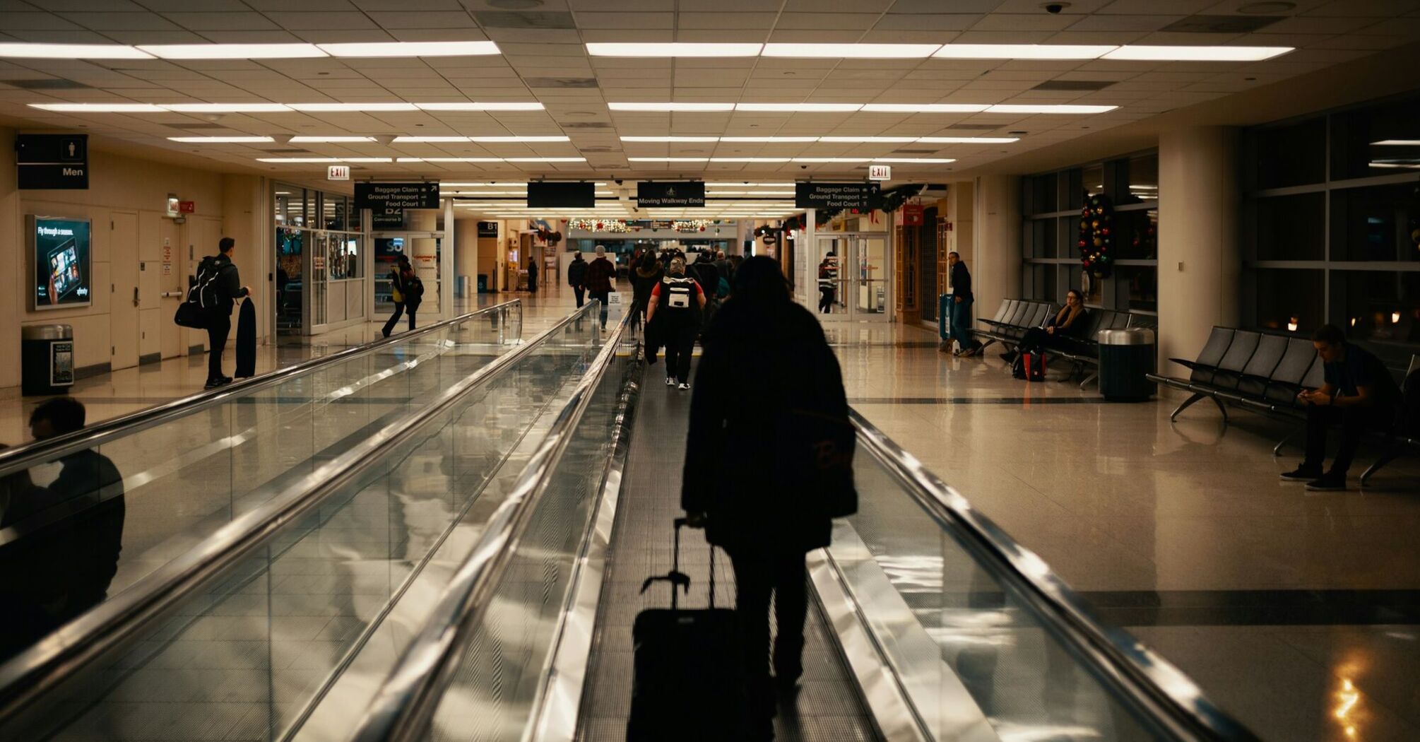 Passenger walking through airport corridor with rolling suitcase