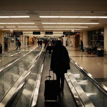 Passenger walking through airport corridor with rolling suitcase