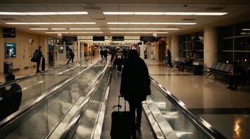 Passenger walking through airport corridor with rolling suitcase