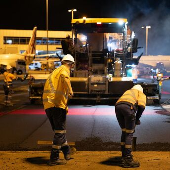 Airport workers resurfacing runway at night near terminal