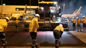 Airport workers resurfacing runway at night near terminal