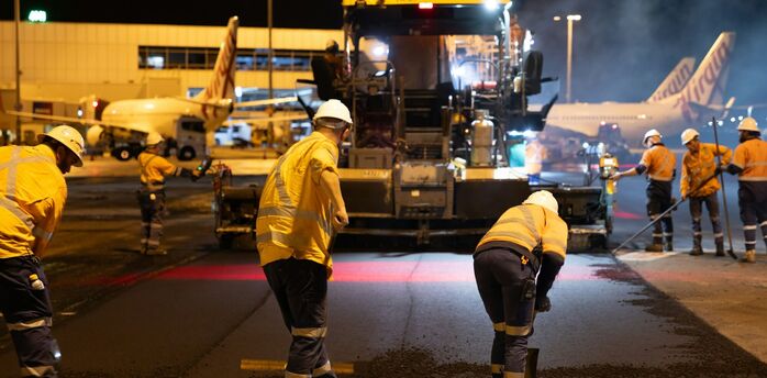 Airport workers resurfacing runway at night near terminal