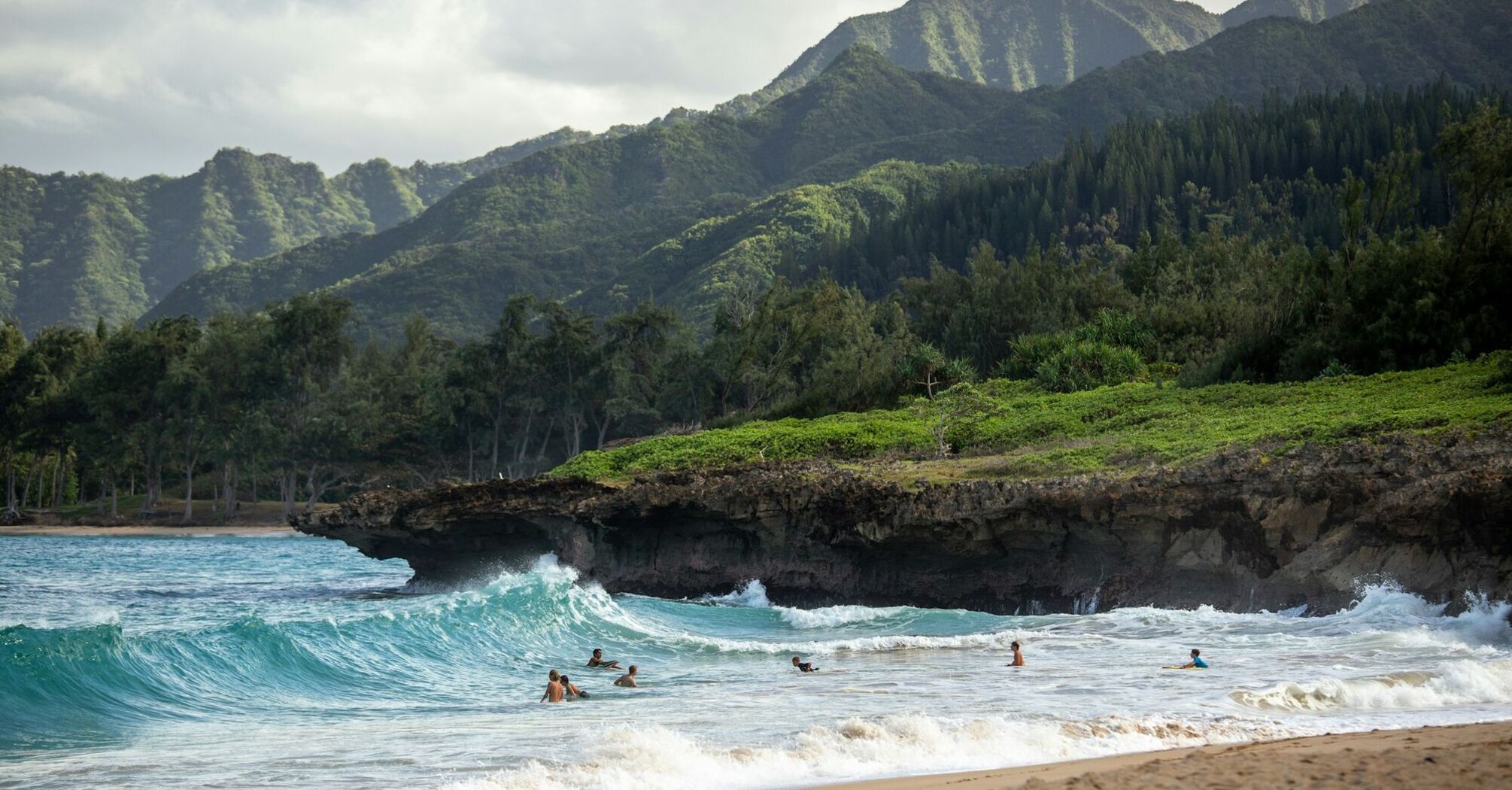 Surfers in ocean waves with green mountains behind on a Hawaii beach