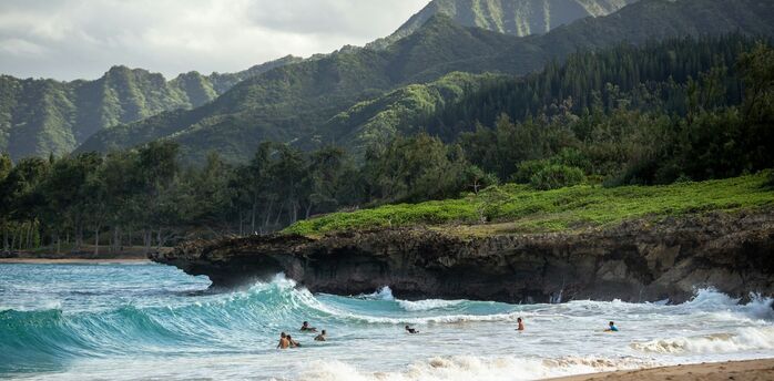 Surfers in ocean waves with green mountains behind on a Hawaii beach