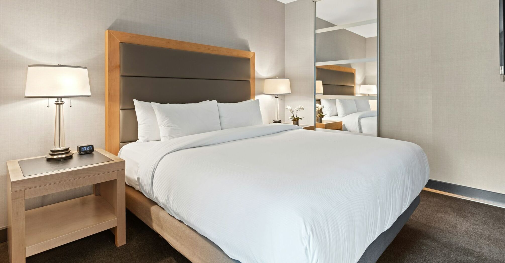 Modern minimalist hotel bedroom with large bed and mirrored wardrobe