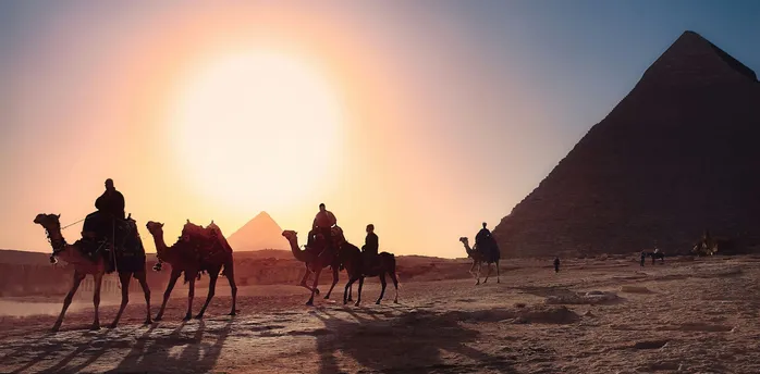 Camel riders near the pyramids at sunset