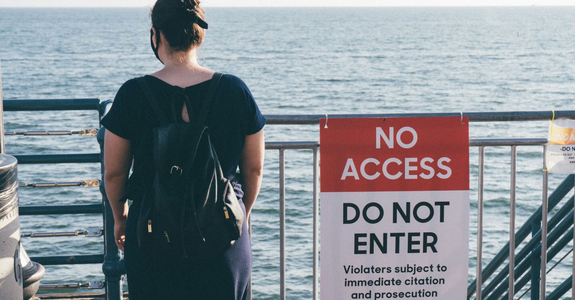 Woman standing near a “No Access” sign by the sea