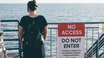 Woman standing near a “No Access” sign by the sea
