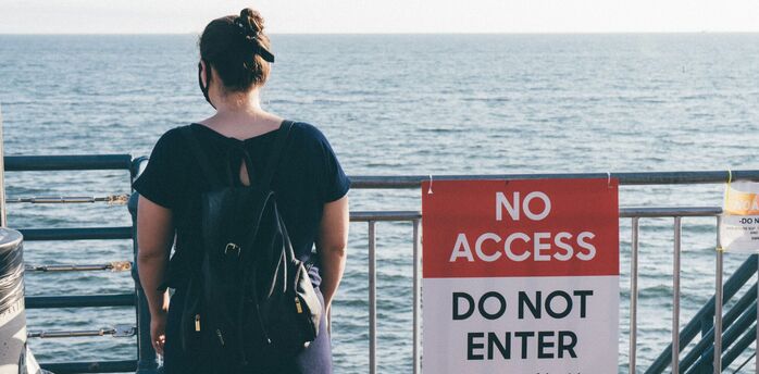 Woman standing near a “No Access” sign by the sea