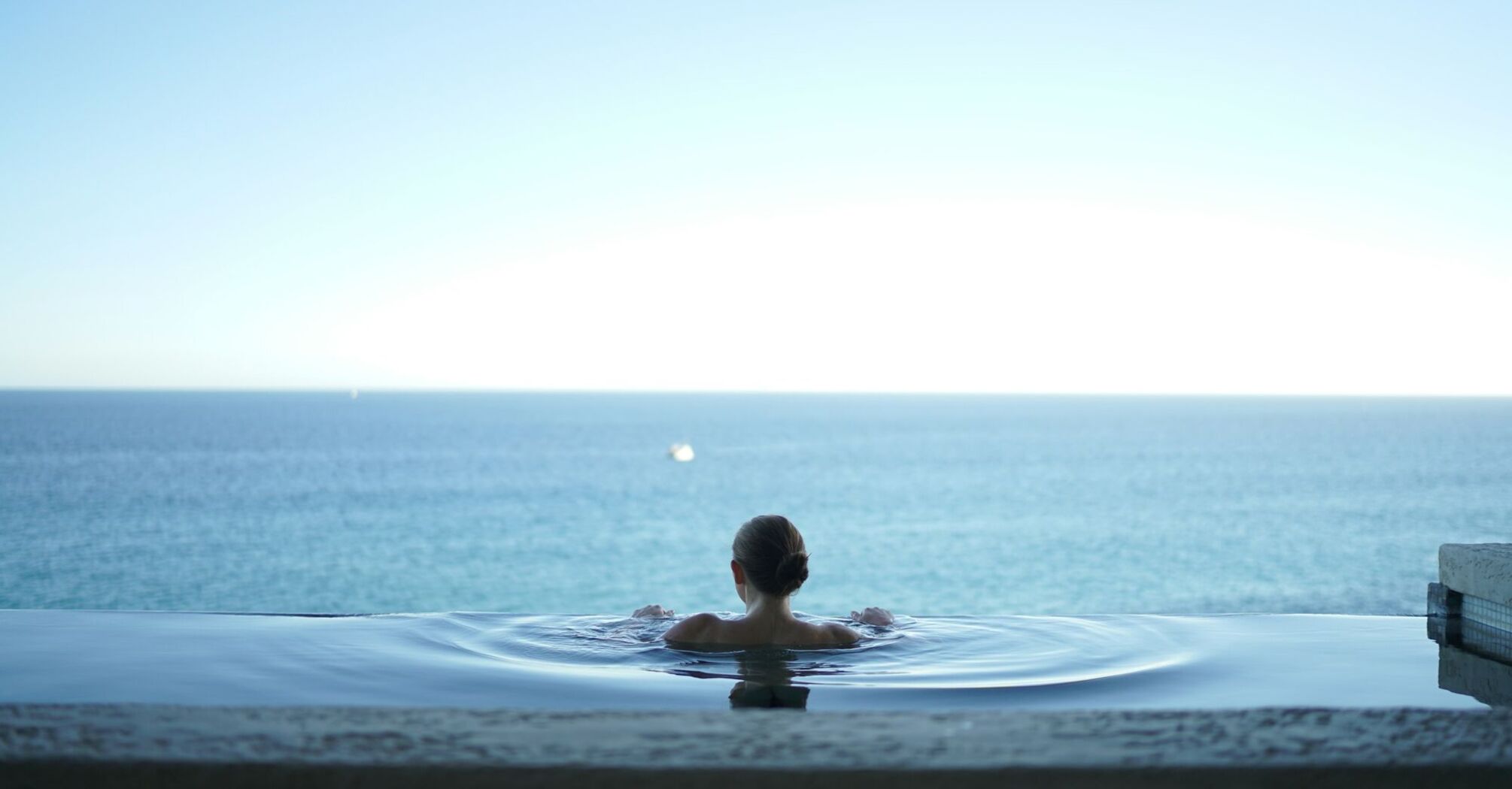 Person relaxing in infinity spa pool overlooking sea