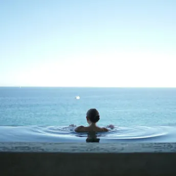 Person relaxing in infinity spa pool overlooking sea