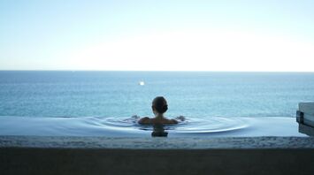 Person relaxing in infinity spa pool overlooking sea