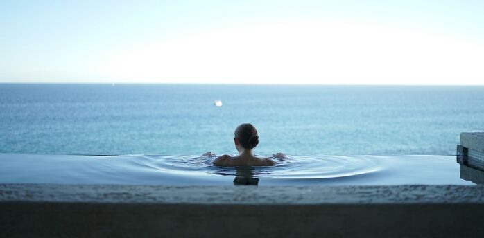 Person relaxing in infinity spa pool overlooking sea