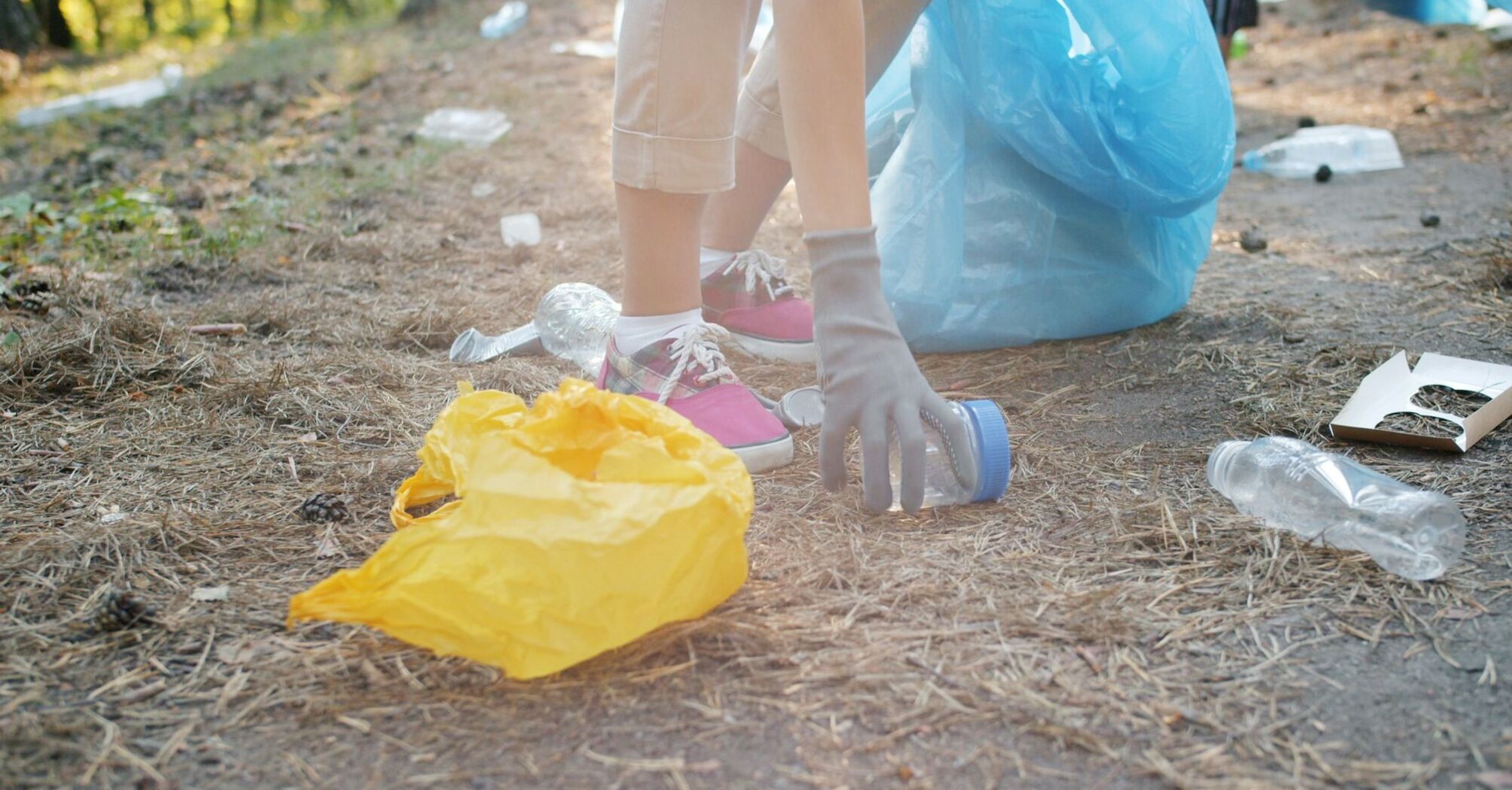 Person picking up plastic waste outdoors with gloves