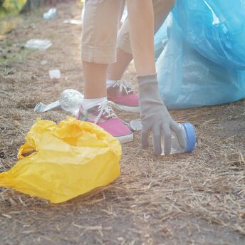 Person picking up plastic waste outdoors with gloves