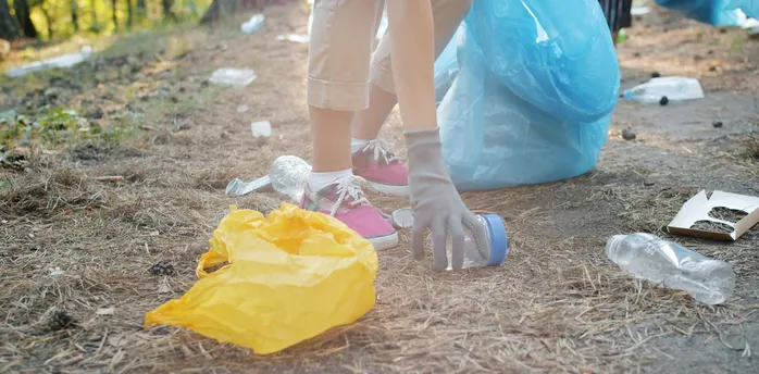 Person picking up plastic waste outdoors with gloves