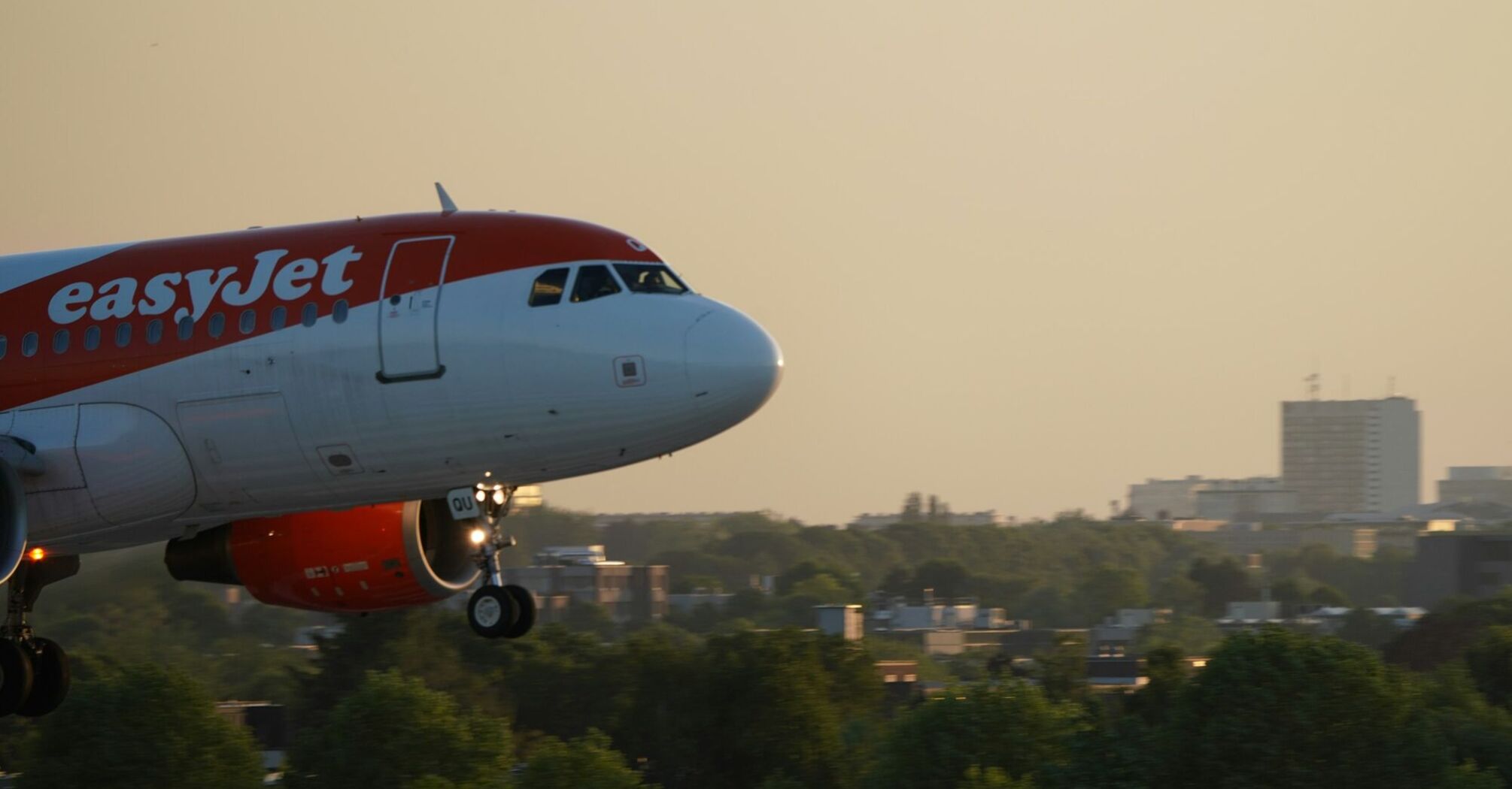 easyJet aircraft flying over city landscape at sunset