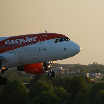 easyJet aircraft flying over city landscape at sunset