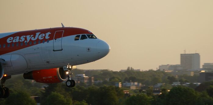 easyJet aircraft flying over city landscape at sunset