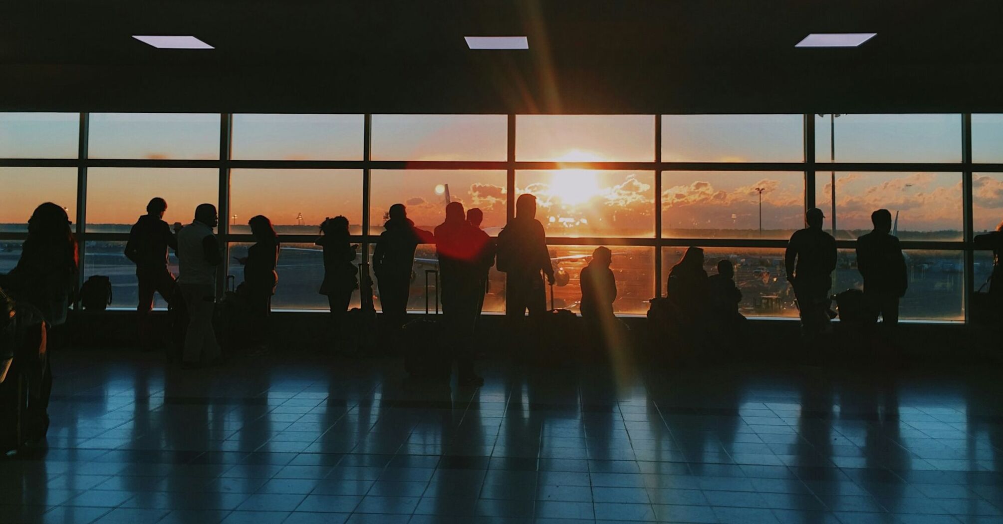 Silhouettes of travellers waiting inside an airport terminal at sunset