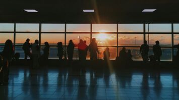 Silhouettes of travellers waiting inside an airport terminal at sunset