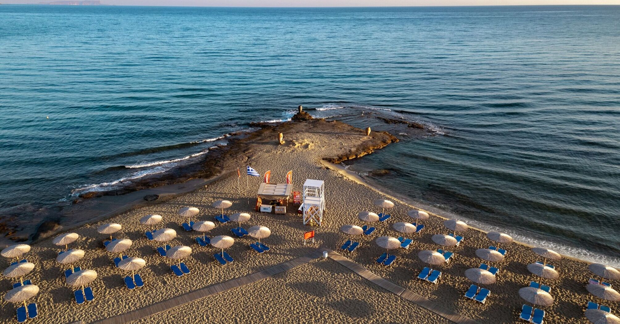 Sandy beach with sun loungers, umbrellas and lifeguard tower on a narrow peninsula