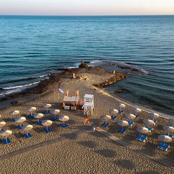 Sandy beach with sun loungers, umbrellas and lifeguard tower on a narrow peninsula