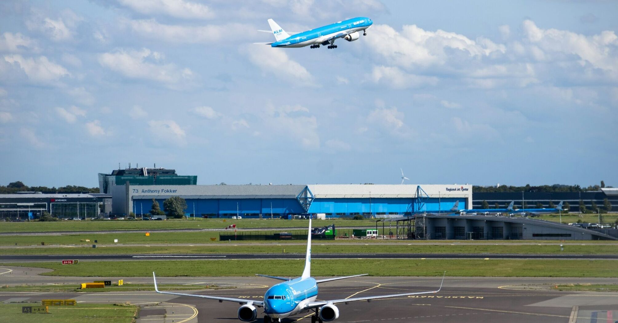 KLM plane taking off above airport buildings under cloudy sky