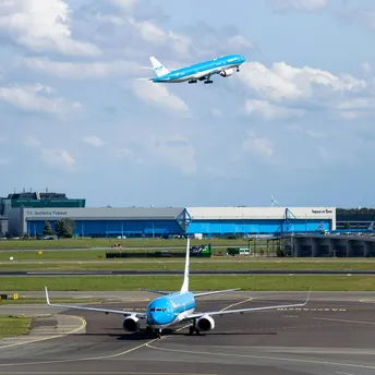 KLM plane taking off above airport buildings under cloudy sky