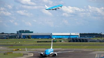 KLM plane taking off above airport buildings under cloudy sky