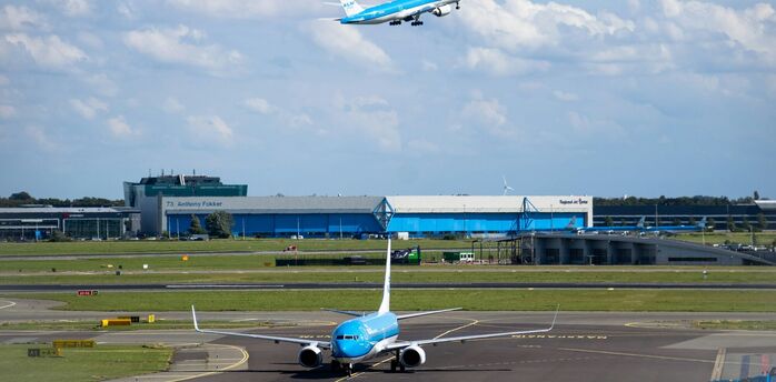 KLM plane taking off above airport buildings under cloudy sky