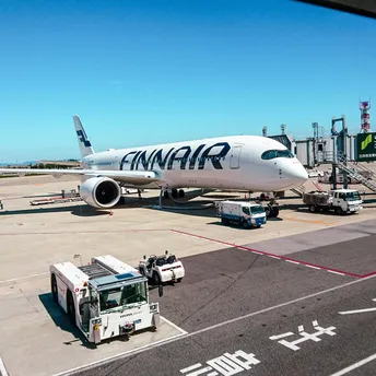 Finnair aircraft parked at airport gate with ground vehicles nearby