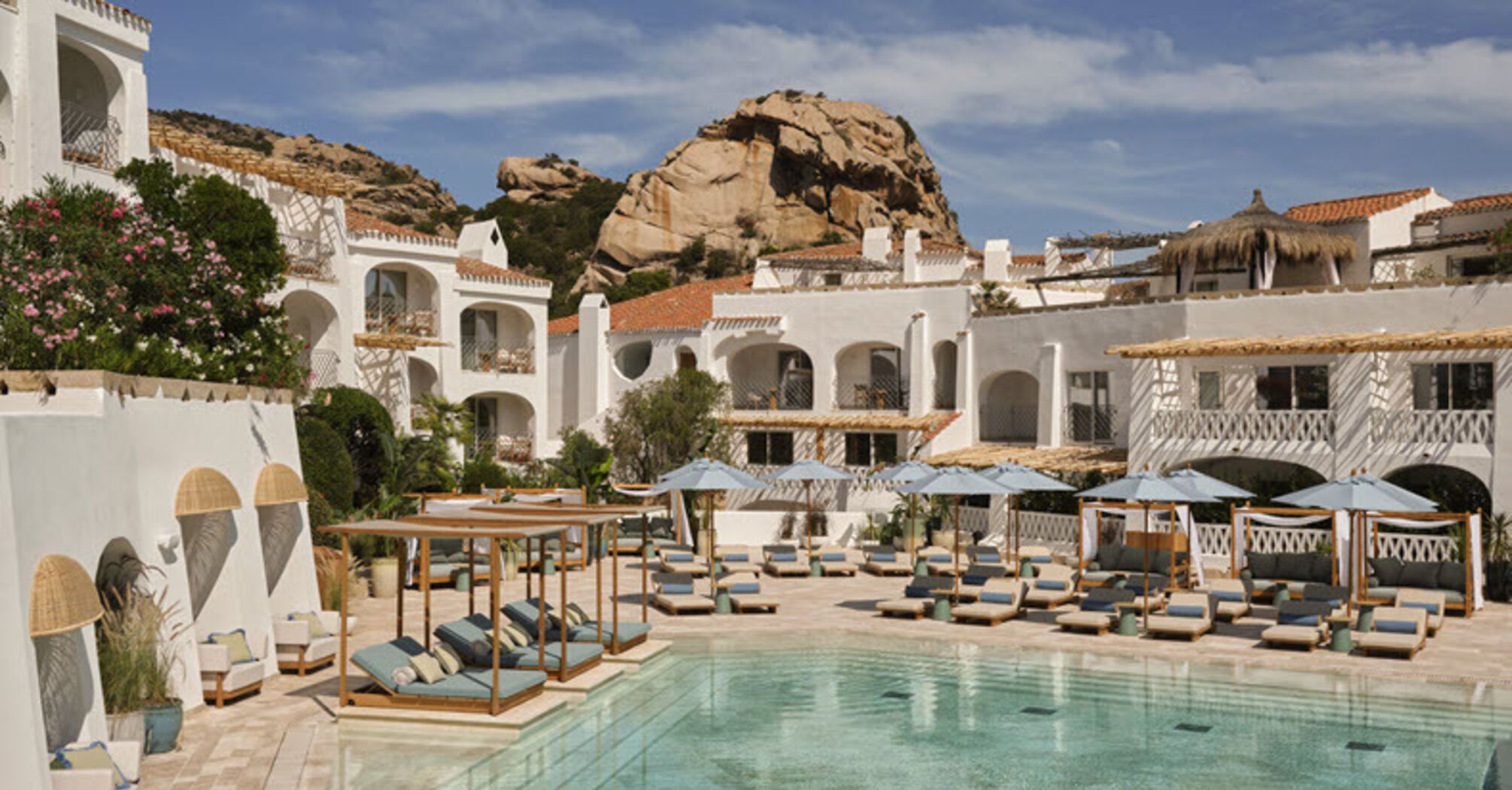 Resort pool courtyard with white buildings and sun loungers in Poltu Quatu