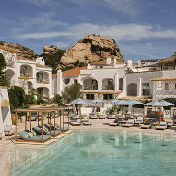 Resort pool courtyard with white buildings and sun loungers in Poltu Quatu