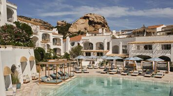 Resort pool courtyard with white buildings and sun loungers in Poltu Quatu