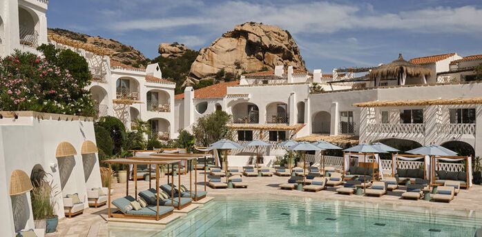Resort pool courtyard with white buildings and sun loungers in Poltu Quatu