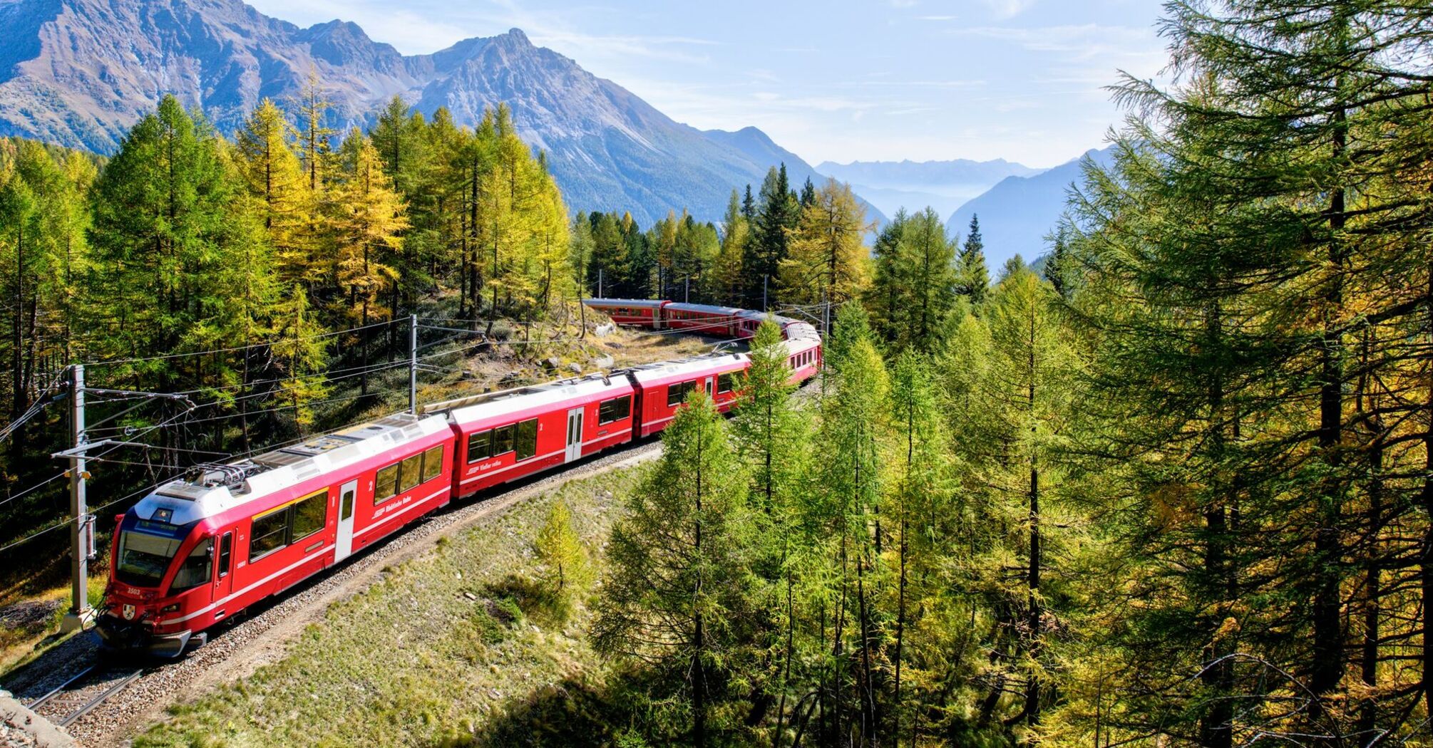 Red train travelling through Alpine mountains