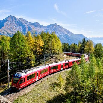 Red train travelling through Alpine mountains